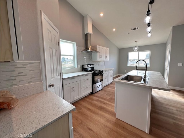 kitchen with stainless steel gas stove, decorative light fixtures, a center island with sink, and sink