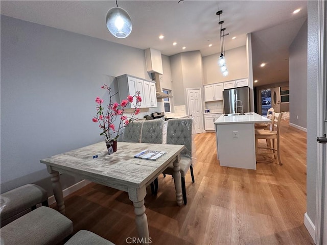 dining room featuring light wood-type flooring, sink, and a high ceiling