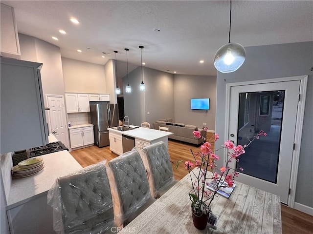 kitchen featuring tasteful backsplash, stainless steel appliances, a center island with sink, white cabinetry, and hanging light fixtures