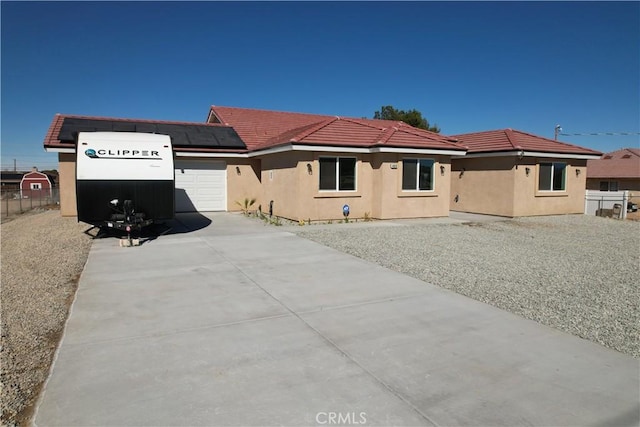 single story home with an attached garage, solar panels, a tiled roof, driveway, and stucco siding