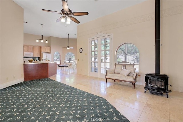 interior space featuring a wood stove, ceiling fan, a high ceiling, and light tile patterned flooring