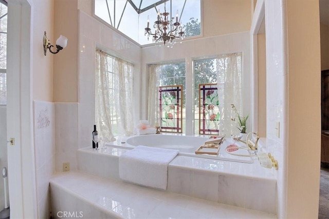 bathroom with tiled tub and a notable chandelier