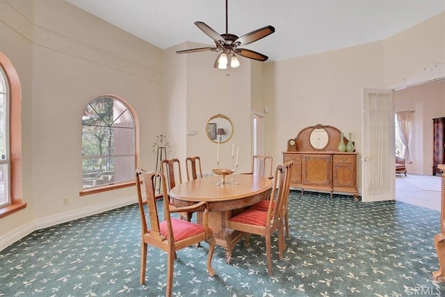 dining area featuring ceiling fan, a towering ceiling, and dark carpet