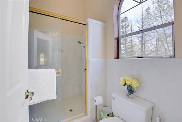 bathroom with tile walls, toilet, and a shower with shower door