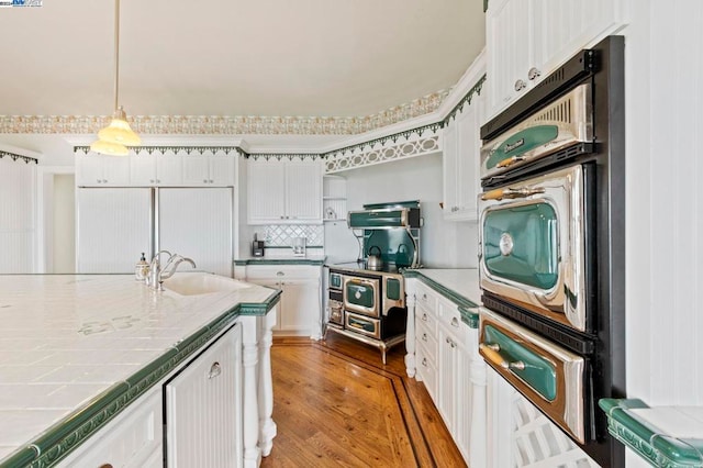 kitchen featuring sink, decorative light fixtures, hardwood / wood-style flooring, white cabinets, and tile counters