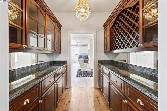 bar featuring a chandelier, pendant lighting, light wood-type flooring, and dark stone countertops