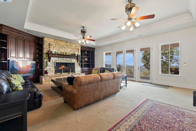 living room featuring a raised ceiling, ceiling fan, a fireplace, and light colored carpet