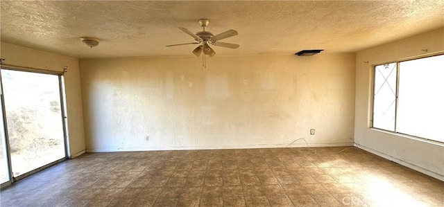 empty room with a wealth of natural light, ceiling fan, and a textured ceiling