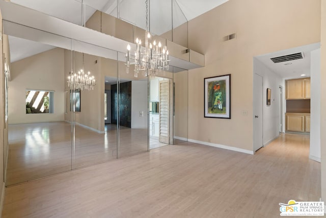 unfurnished dining area featuring an inviting chandelier, light hardwood / wood-style floors, and high vaulted ceiling