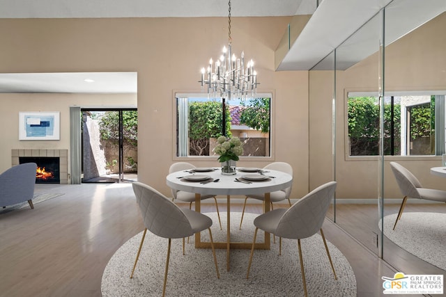 dining area with a tiled fireplace, a chandelier, and hardwood / wood-style flooring