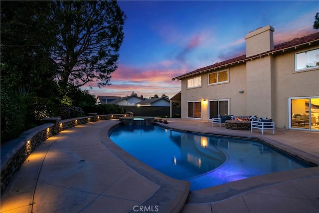 pool at dusk featuring a patio area and an in ground hot tub