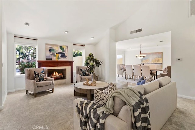 carpeted living room featuring a fireplace, lofted ceiling, a healthy amount of sunlight, and a notable chandelier