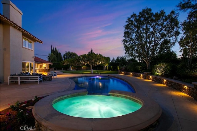 pool at dusk with an in ground hot tub and a patio