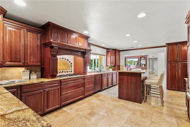 kitchen with light stone countertops, tasteful backsplash, a breakfast bar, stainless steel gas cooktop, and sink