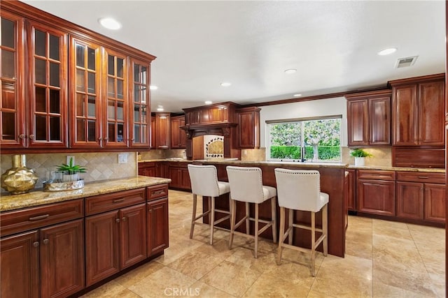 kitchen featuring light stone countertops, backsplash, ornamental molding, a breakfast bar, and a kitchen island