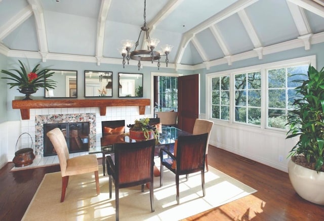 dining room featuring a notable chandelier, wood-type flooring, vaulted ceiling with beams, and a tile fireplace