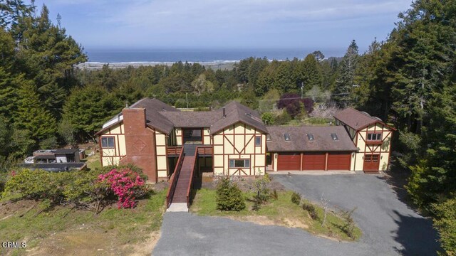 view of front of property featuring a garage, a water view, driveway, and a view of trees