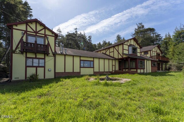 rear view of house with a yard, roof with shingles, a balcony, and stucco siding