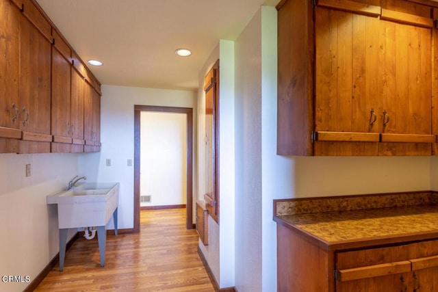 kitchen featuring light wood-style flooring, brown cabinets, baseboards, and visible vents