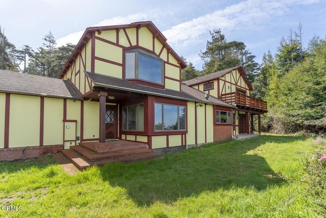 rear view of house featuring a shingled roof, a lawn, stucco siding, brick siding, and a wooden deck