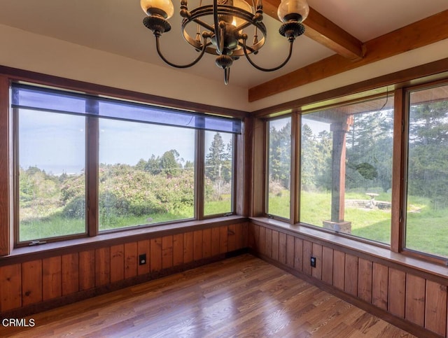 unfurnished sunroom featuring beamed ceiling, a notable chandelier, wood finished floors, and wood walls