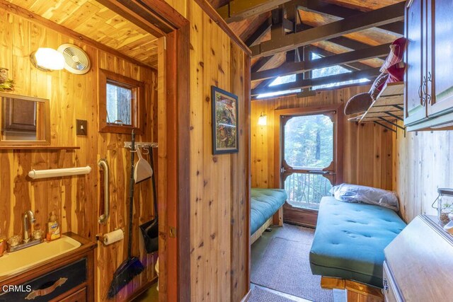 interior space with a sink, wood walls, vaulted ceiling with beams, and indoor wet bar