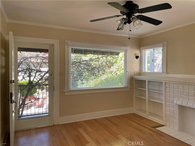 doorway featuring crown molding, ceiling fan, a tile fireplace, and light wood-type flooring