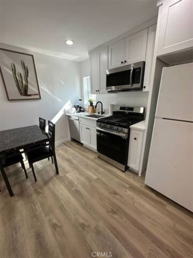 kitchen with sink, appliances with stainless steel finishes, light hardwood / wood-style flooring, and white cabinets