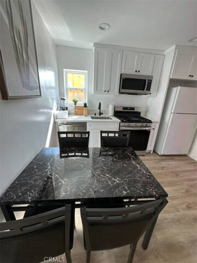 kitchen with sink, white cabinetry, stainless steel appliances, dark stone countertops, and light hardwood / wood-style flooring