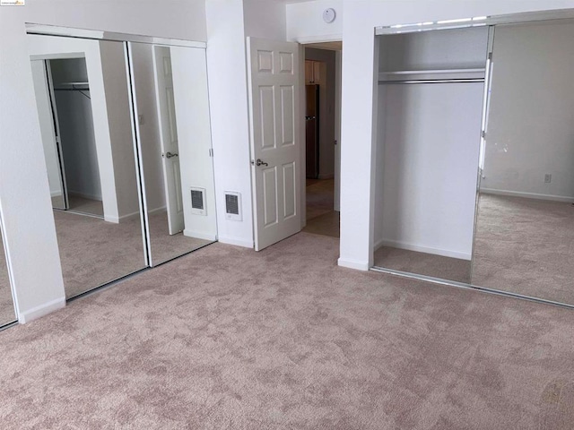 unfurnished bedroom with stainless steel fridge, multiple closets, and light carpet