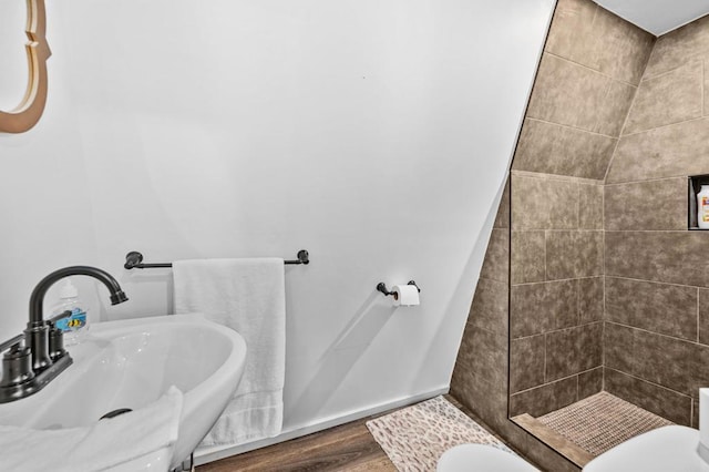 bathroom with wood-type flooring, a tile shower, toilet, and sink