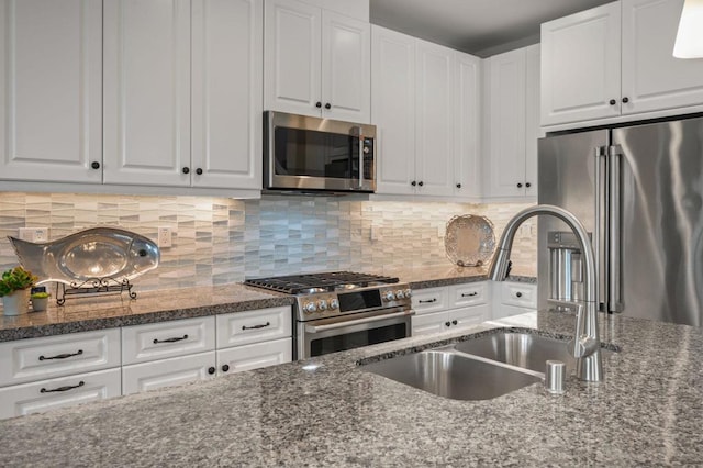 kitchen featuring sink, appliances with stainless steel finishes, white cabinetry, backsplash, and dark stone counters