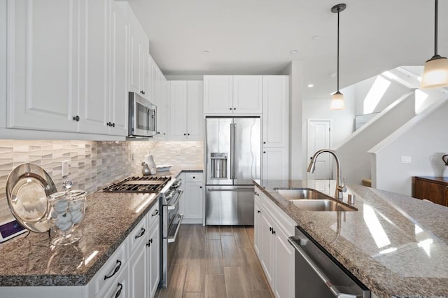 kitchen featuring sink, white cabinetry, premium appliances, a center island with sink, and decorative light fixtures