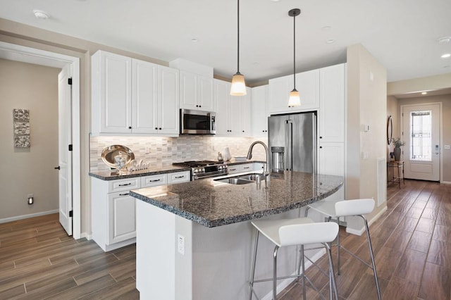 kitchen with sink, dark stone countertops, white cabinets, high end appliances, and a center island with sink