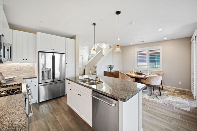 kitchen featuring appliances with stainless steel finishes, decorative light fixtures, white cabinetry, sink, and dark stone countertops