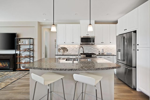 kitchen featuring white cabinetry, hanging light fixtures, a center island with sink, and appliances with stainless steel finishes