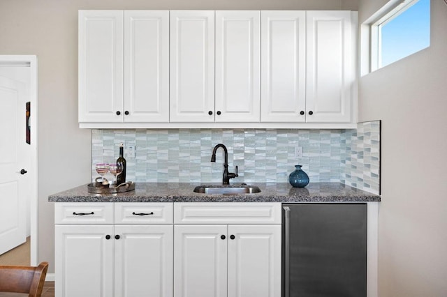 bar featuring stainless steel refrigerator, sink, decorative backsplash, and white cabinets