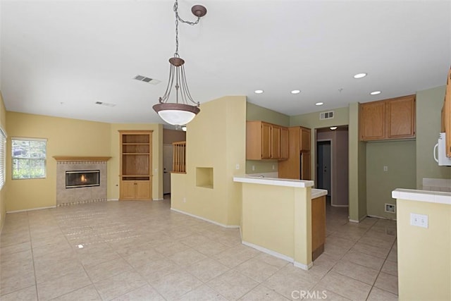 kitchen with light tile patterned flooring, kitchen peninsula, a tile fireplace, and hanging light fixtures