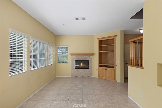 unfurnished living room with a tile fireplace, light tile patterned flooring, and built in shelves