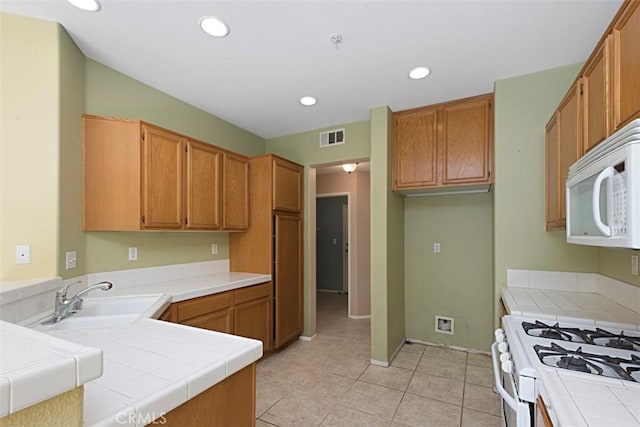 kitchen with sink, white appliances, tile counters, light tile patterned flooring, and kitchen peninsula