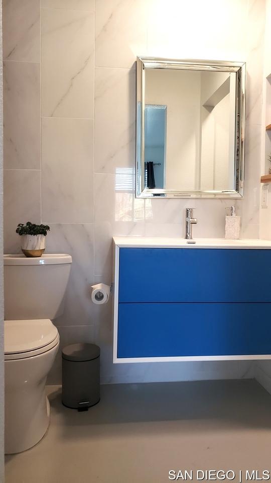 bathroom featuring vanity, tile walls, and toilet