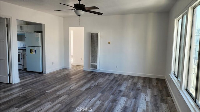 interior space featuring dark wood-type flooring, a ceiling fan, freestanding refrigerator, and baseboards