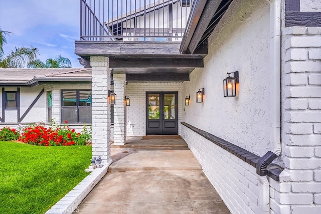 view of exterior entry featuring a balcony, french doors, and a lawn