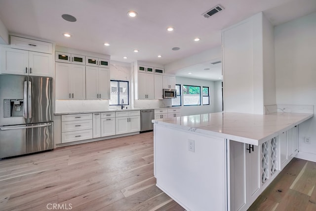 kitchen with white cabinets, light stone counters, stainless steel appliances, light hardwood / wood-style floors, and kitchen peninsula