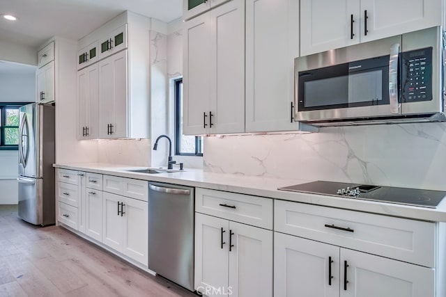 kitchen featuring appliances with stainless steel finishes, tasteful backsplash, light hardwood / wood-style floors, sink, and white cabinetry