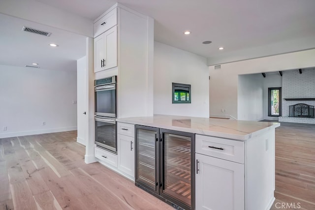 kitchen featuring light wood-type flooring, light stone countertops, white cabinetry, and stainless steel double oven