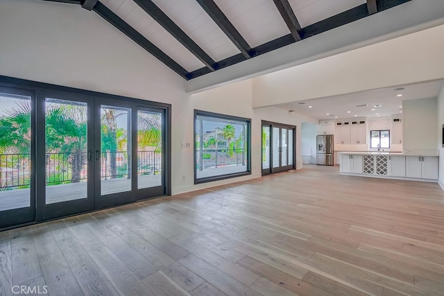 unfurnished living room with high vaulted ceiling, beam ceiling, and light hardwood / wood-style floors