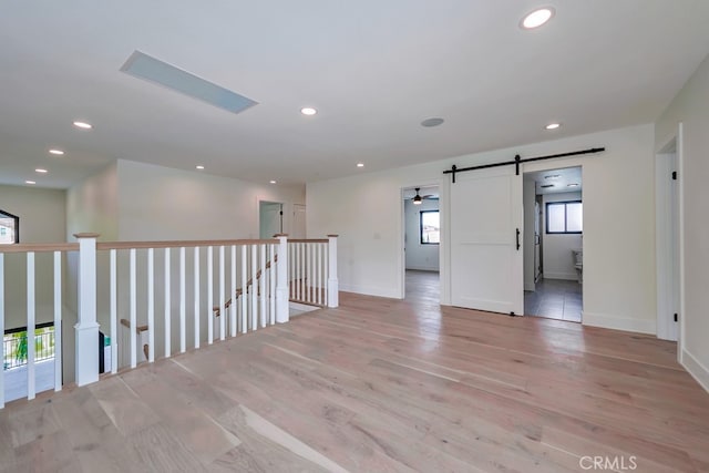 spare room featuring a barn door, a skylight, a wealth of natural light, and light hardwood / wood-style floors