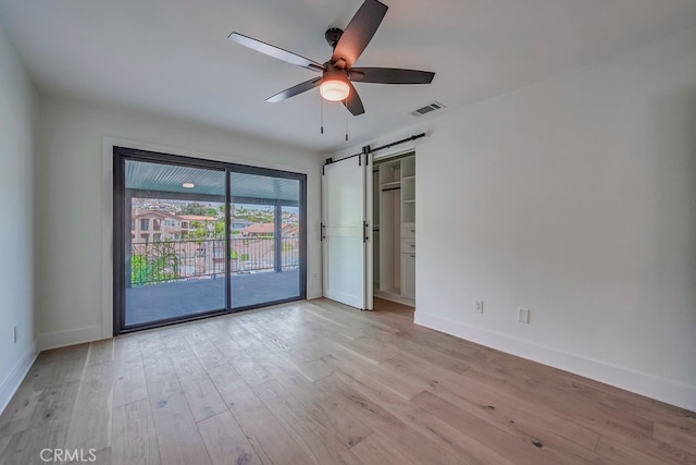 empty room featuring a barn door, ceiling fan, and light wood-type flooring