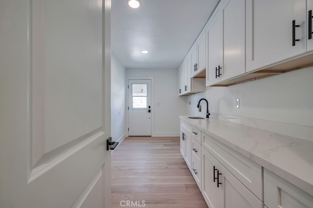 interior space featuring light wood-type flooring, white cabinetry, sink, and light stone countertops